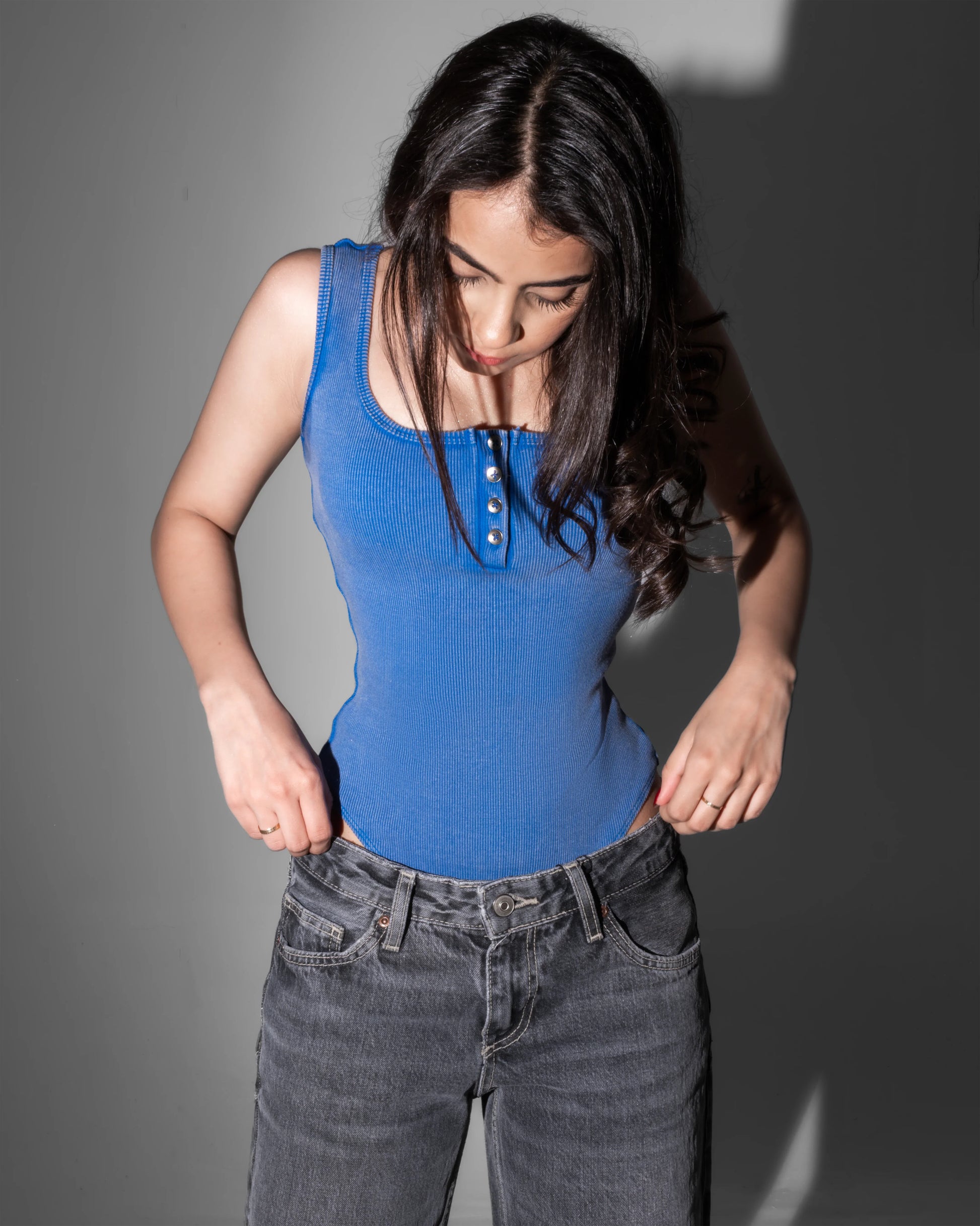Woman wearing a blue tank top and gray jeans against a gray background